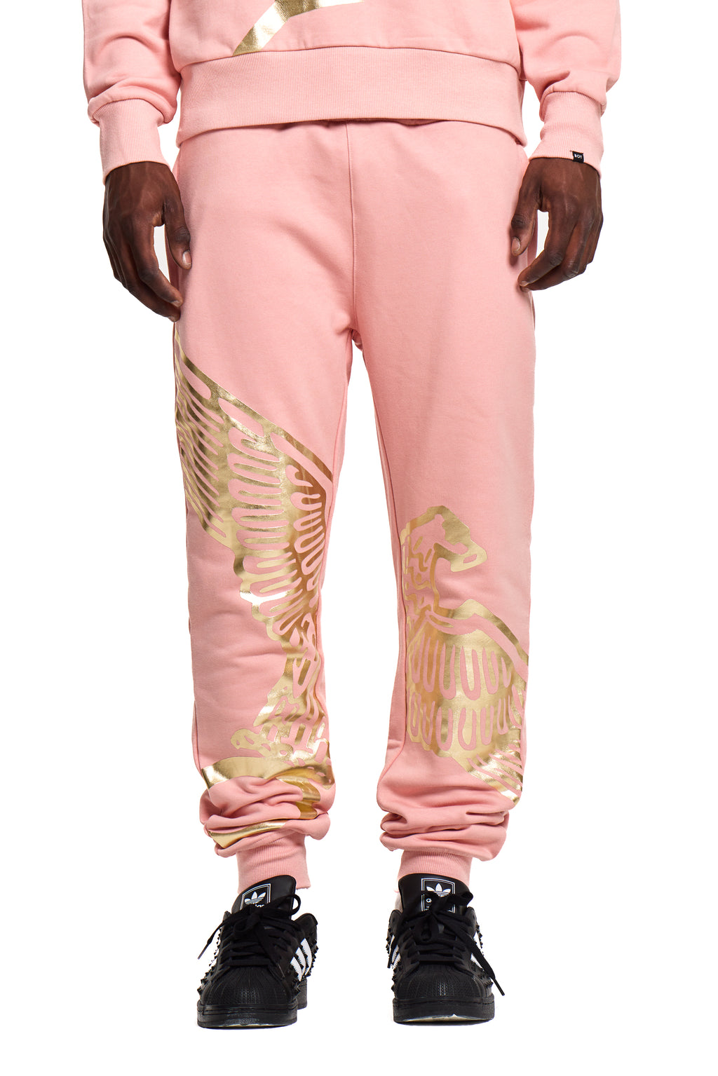 Person wearing pink BOY London sweatpants with gold eagle designs and black sneakers on a white background