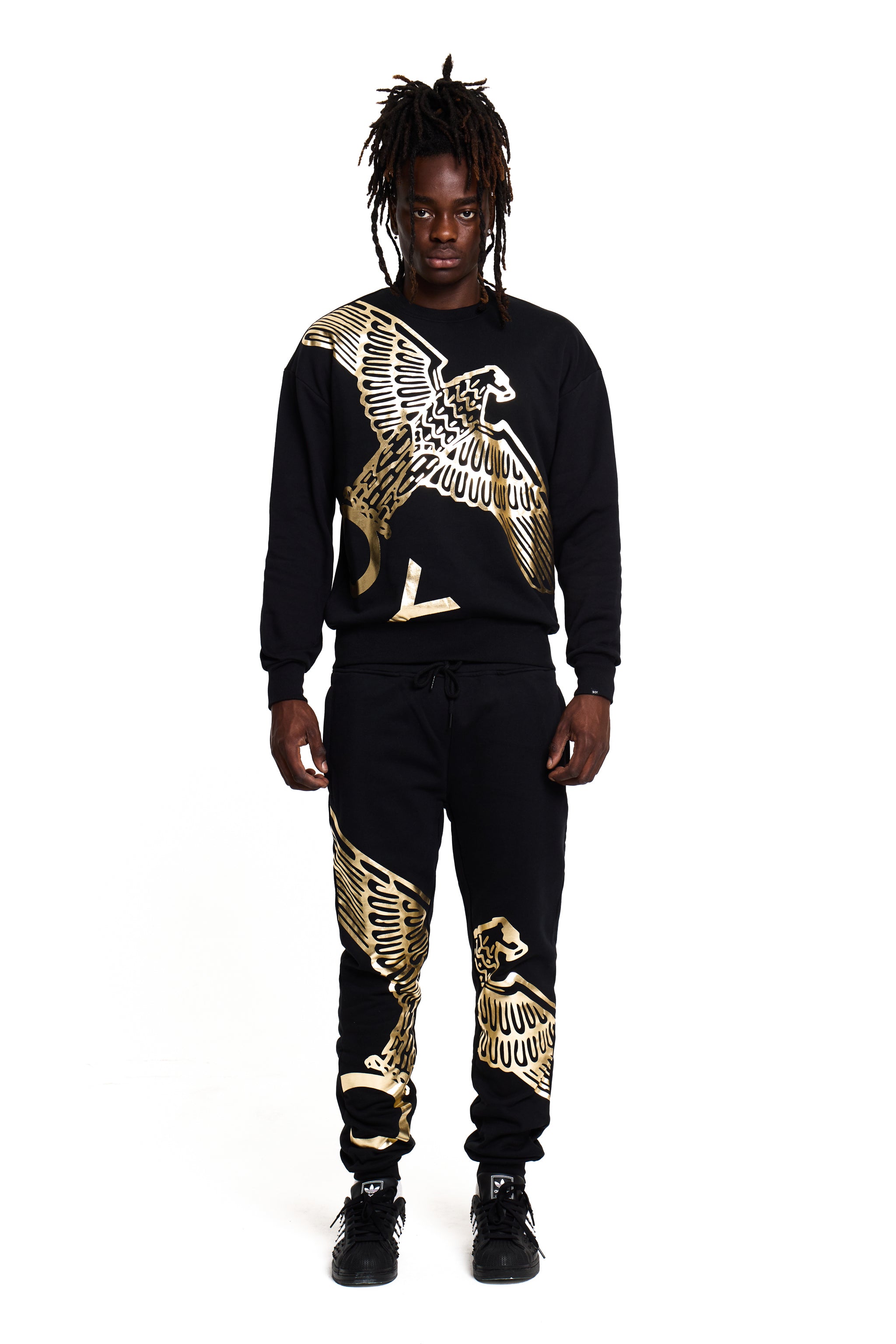 Model wearing a black and gold BOY London tracksuit with eagle designs on a white background