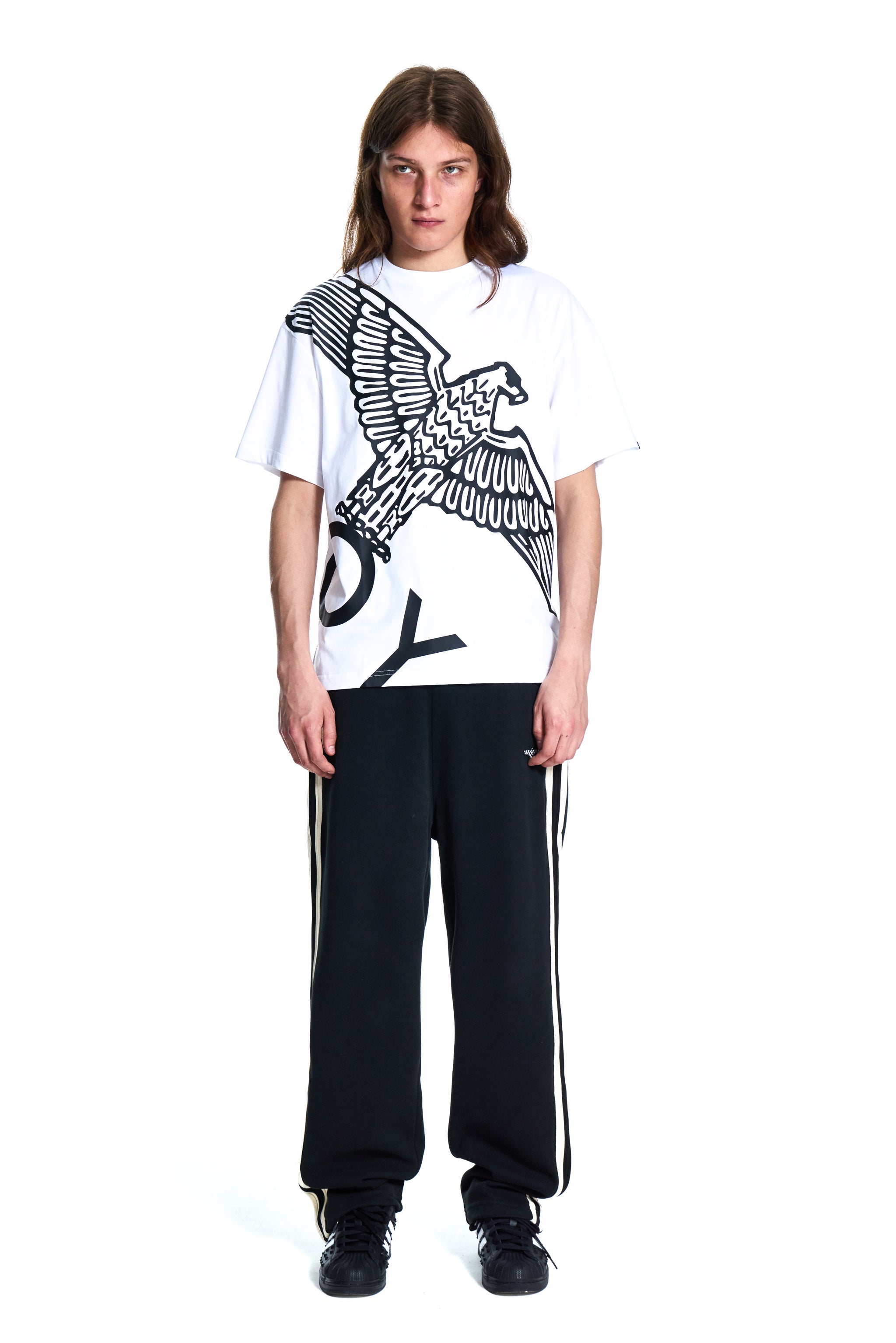 Person wearing a white t-shirt with an eagle design and black pants on a white background