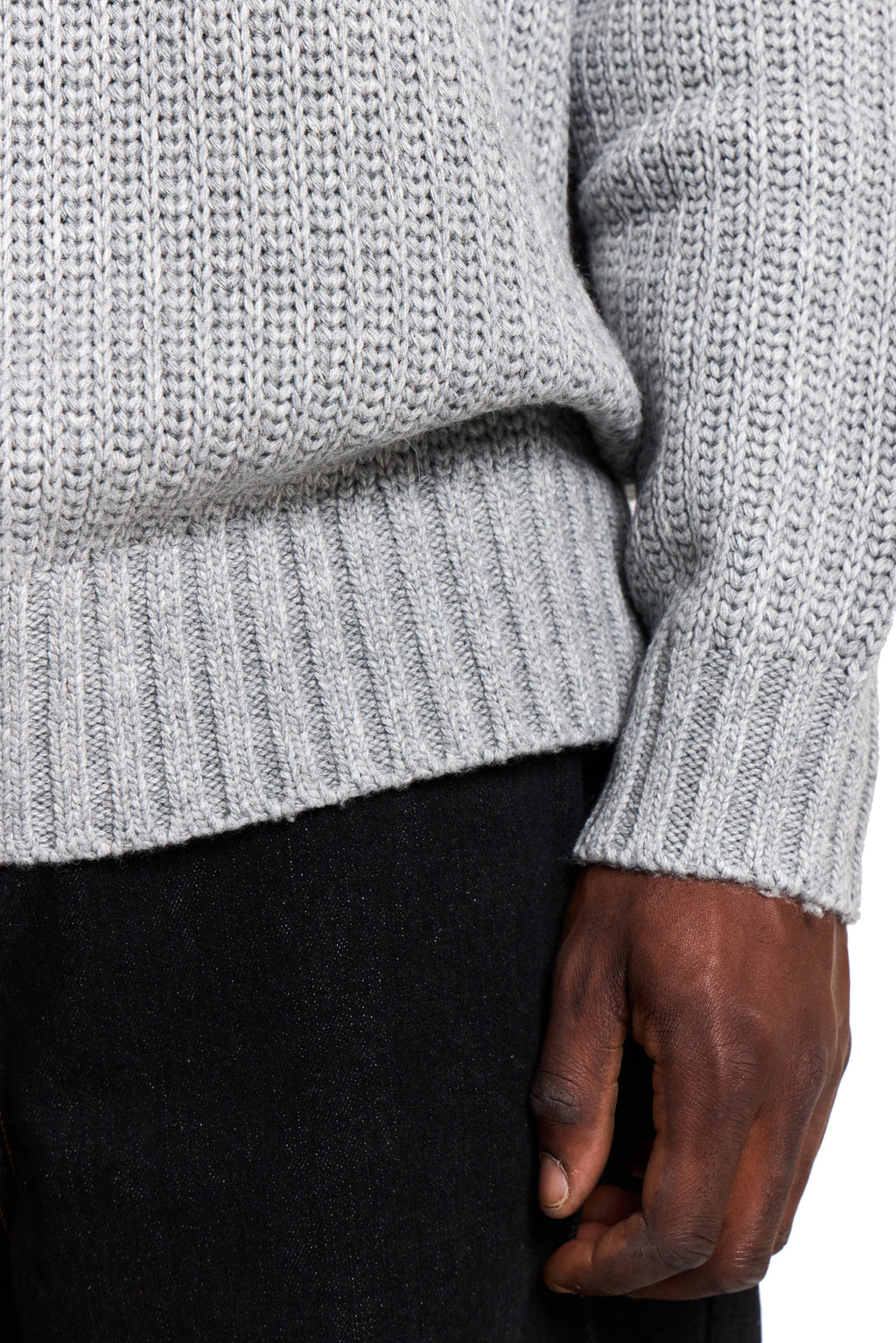 Close-up of a person wearing a light gray knitted sweater with a dark background