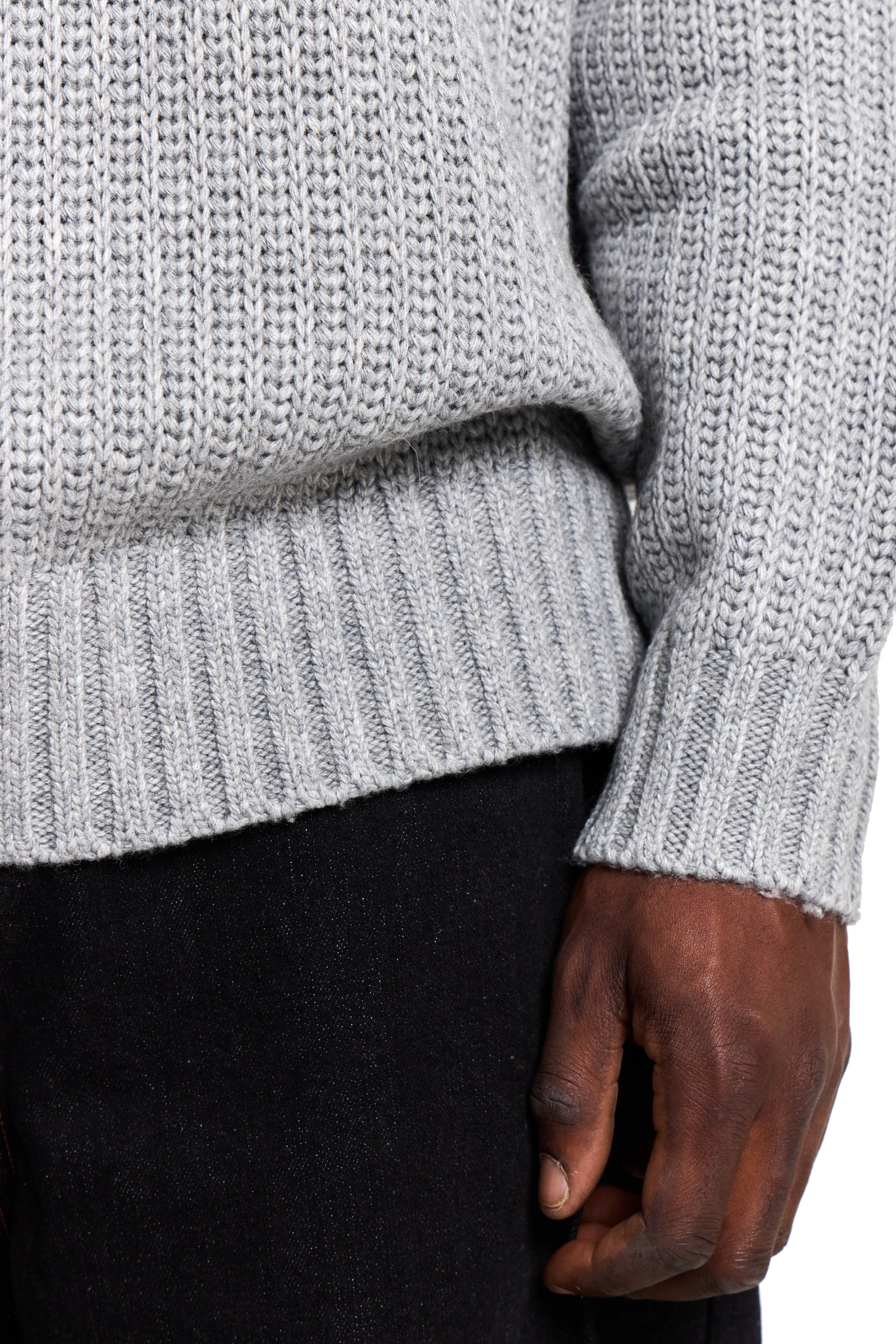 Close-up of a person wearing a light gray knitted sweater with a dark background