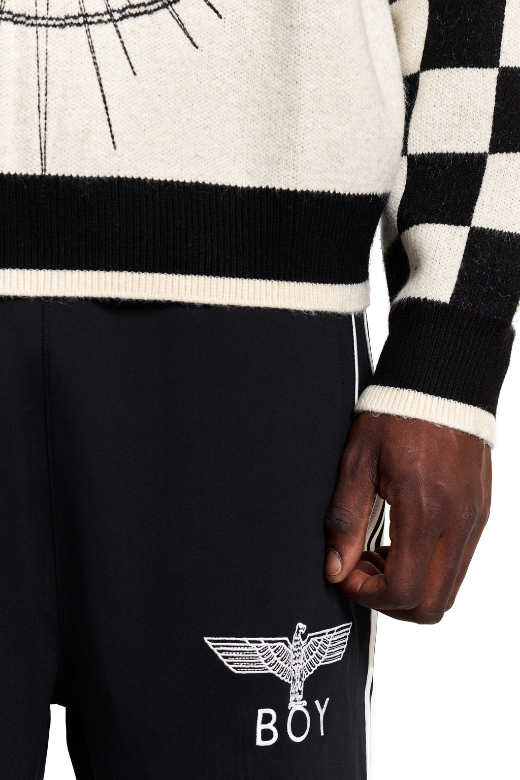 Person wearing a black and white Boy London checkered sweater with a brand logo on black pants.