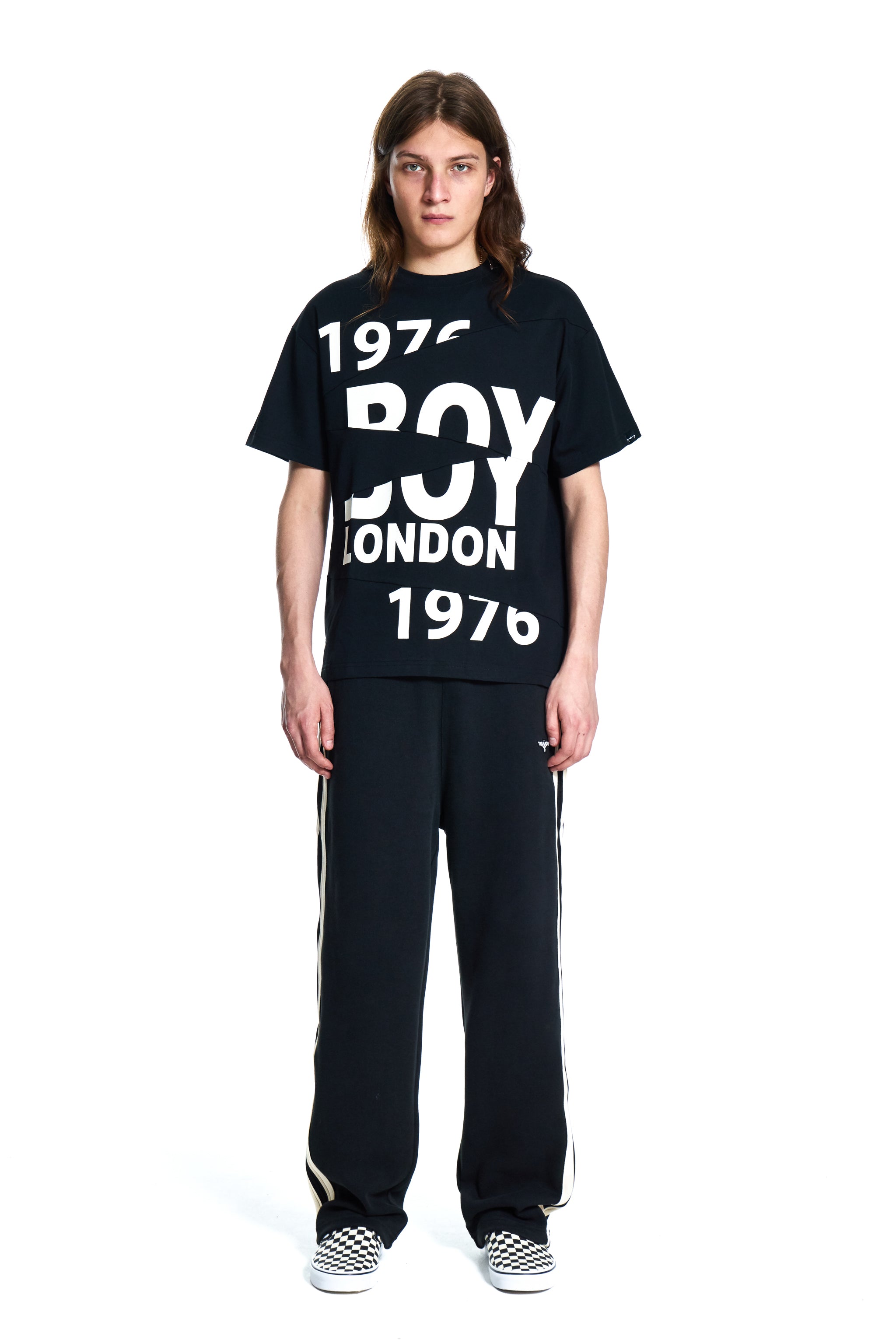 Person wearing a black 'BOY LONDON' t-shirt and black pants with white stripes on a white background