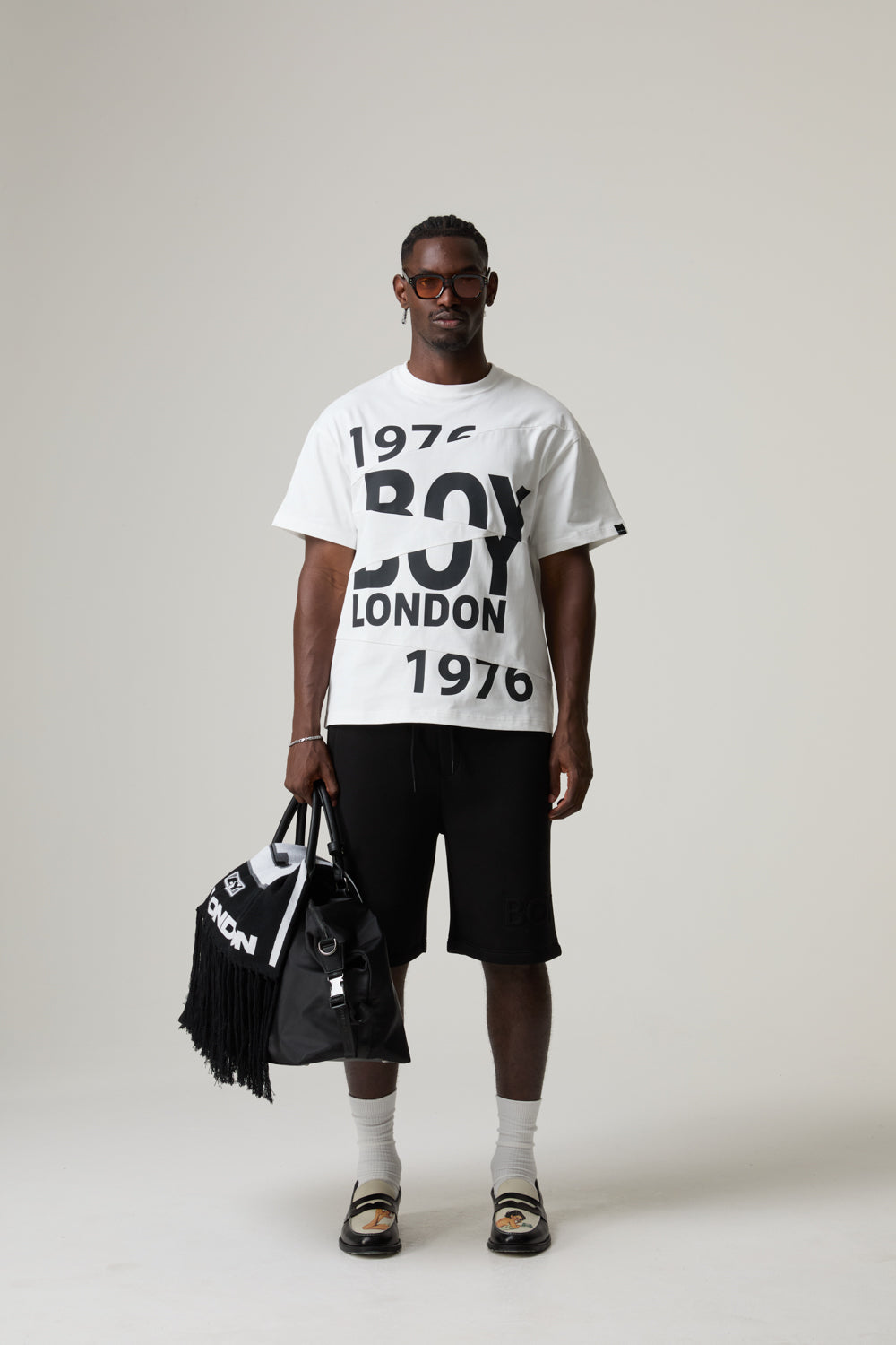 Model wearing a '1976 BOY LONDON' t-shirt holding bags with the brand logo.