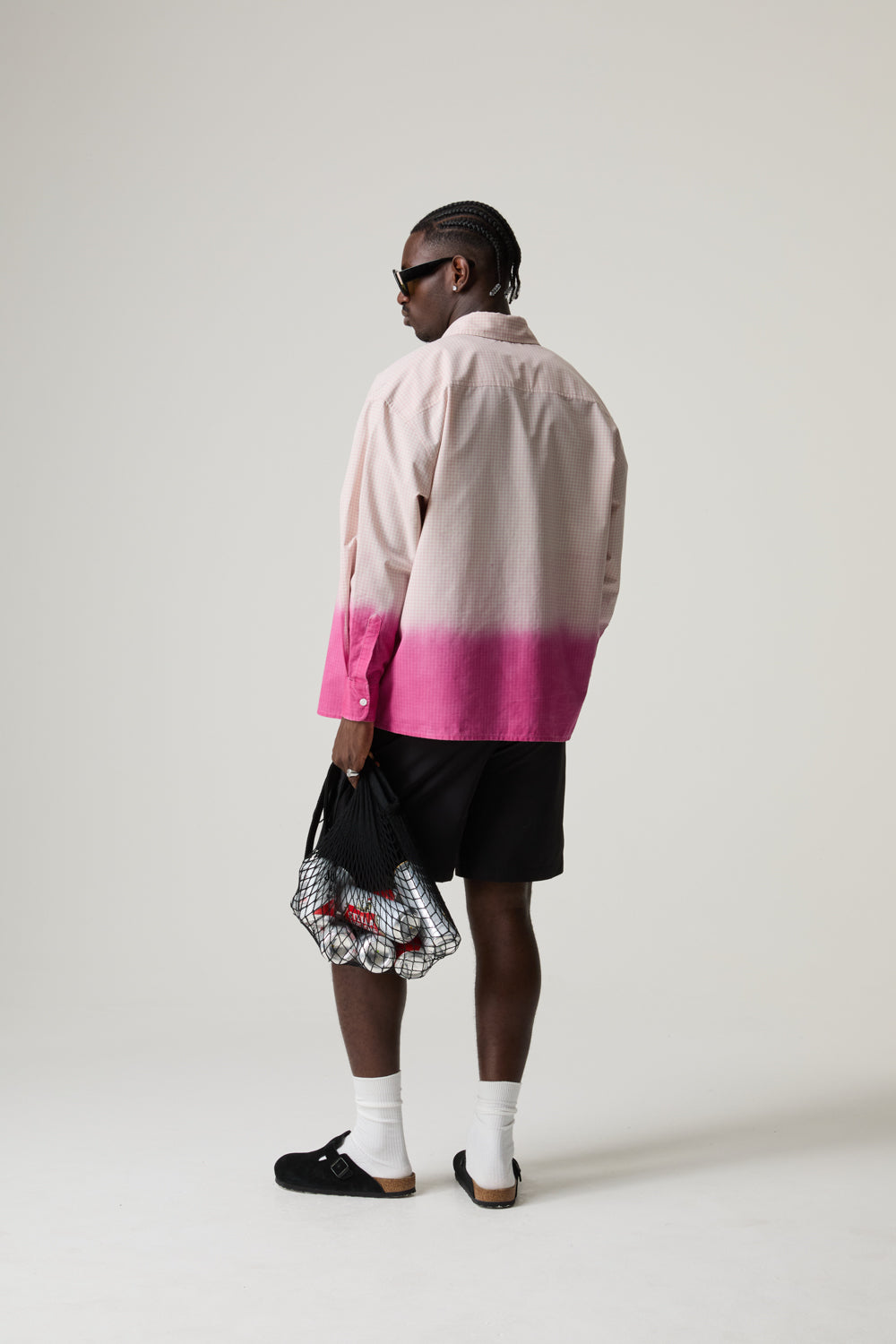 Model wearing a pink and white BOY LONDON gradient shirt with black shorts, holding a patterned bag on a plain background