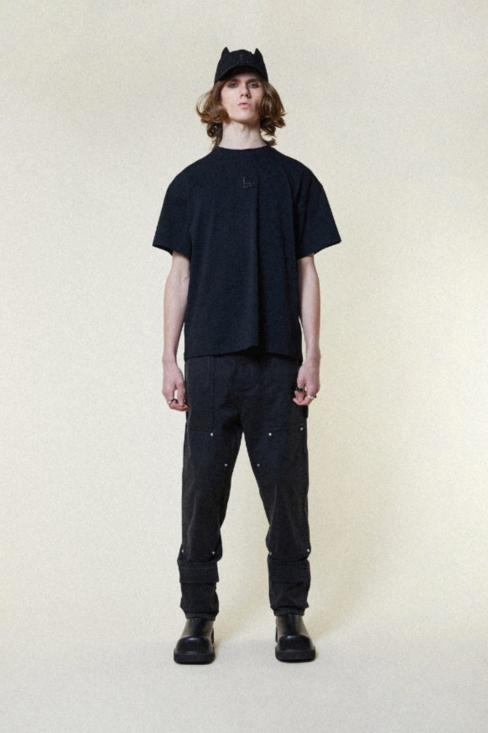 Person wearing a BOY London black t-shirt, pants, and cap on a white background