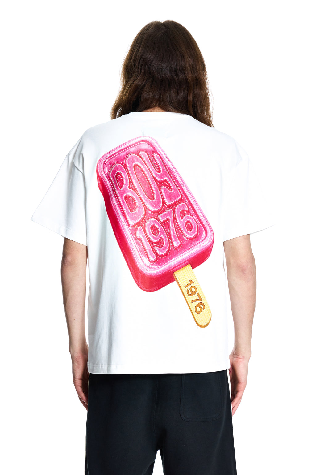 Person wearing a white t-shirt with a pink ice cream popsicle graphic and 'BOY 1976' text on the back.