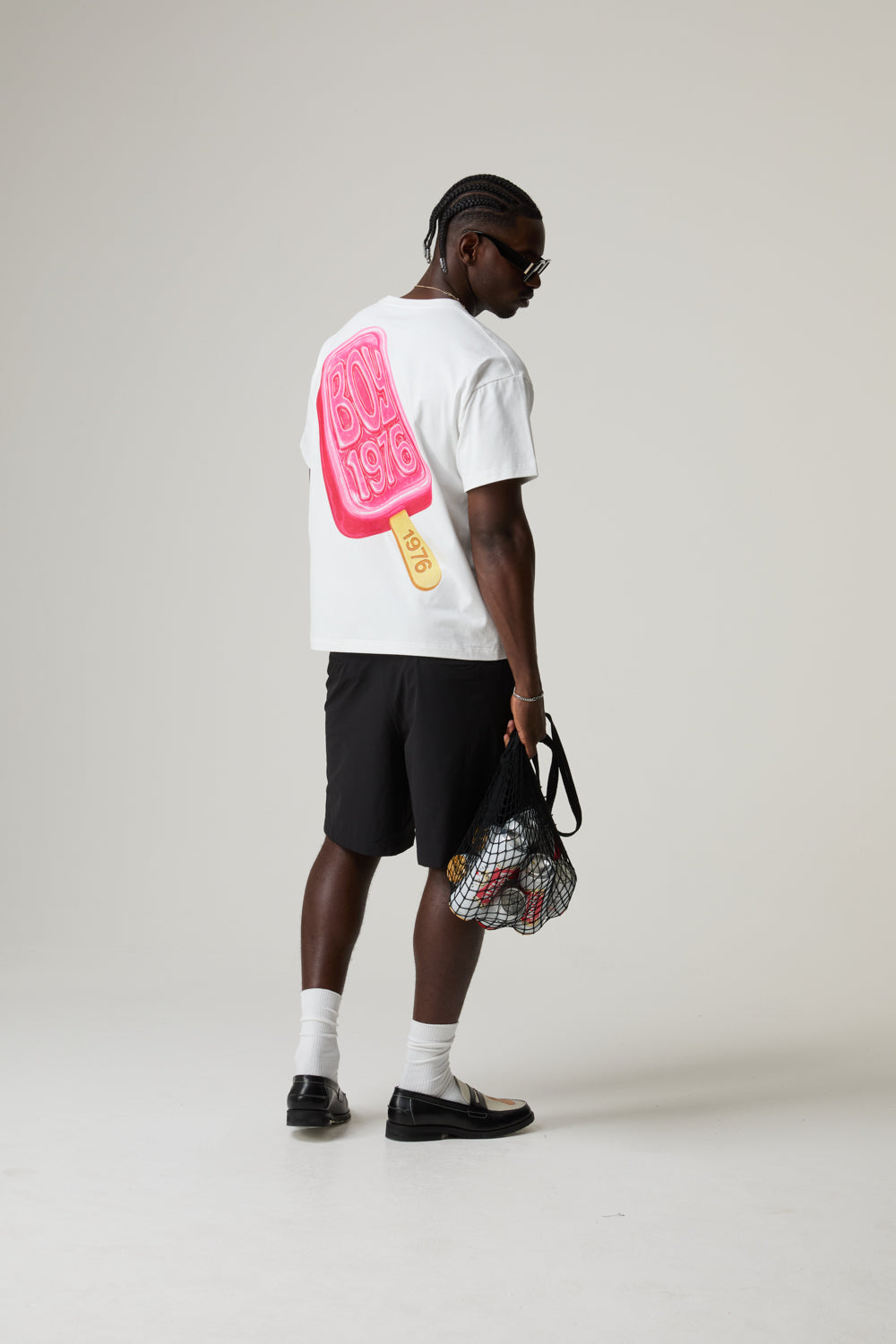 Model wearing a white BOY LONDON t-shirt with a colourful graphic and black shorts on a plain background