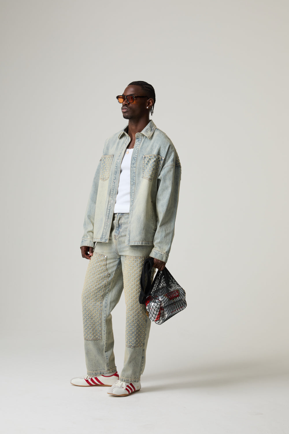 Model wearing a light BOY LONDON denim jacket, white pants, and red and white sneakers on a plain background