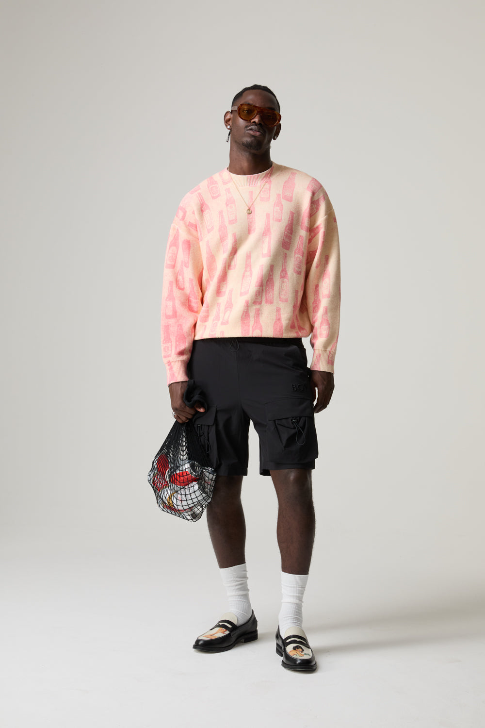 Model wearing a BOY LONDON pink sweater, black shorts, white socks, and sandals on a plain background