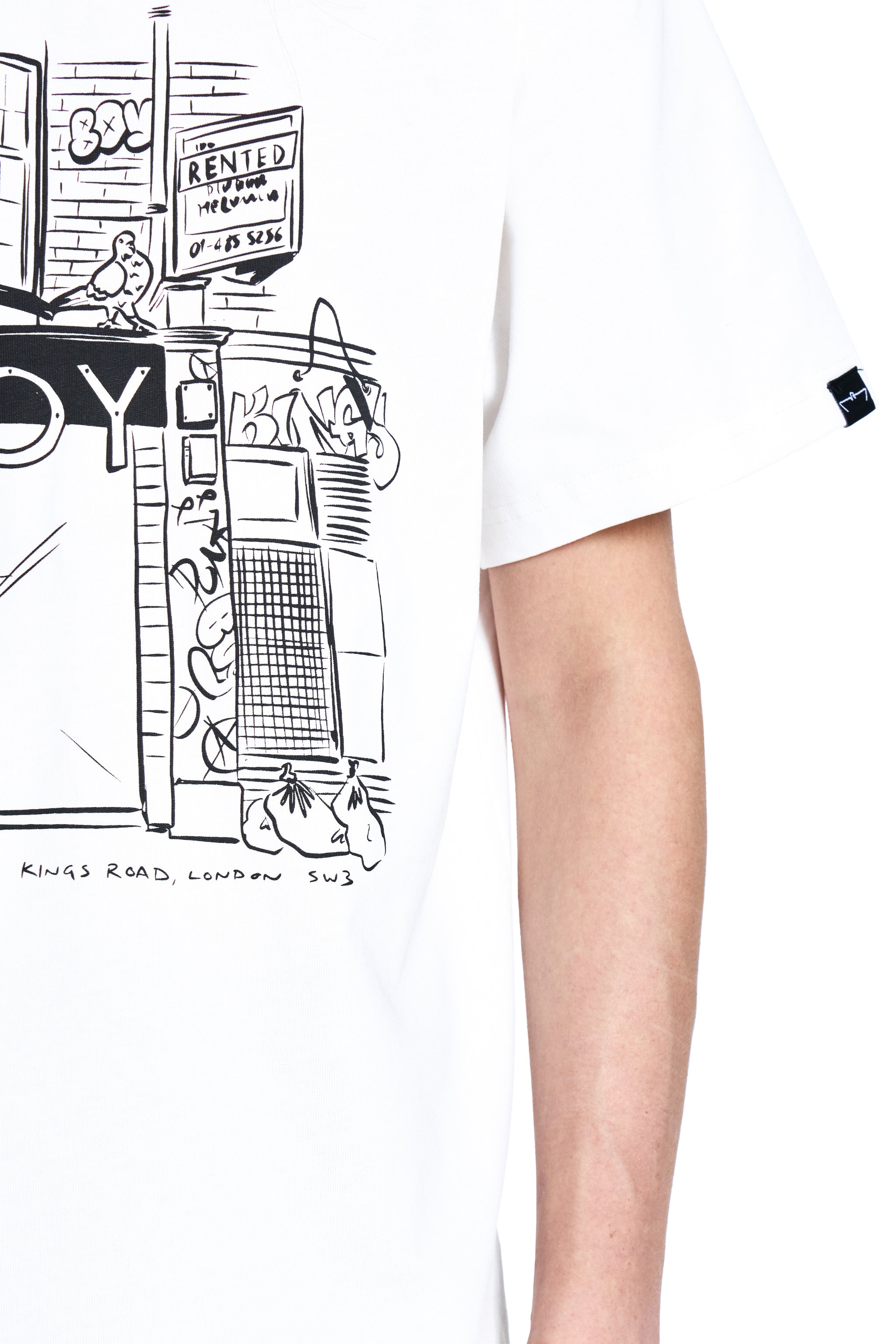 White BOY London t-shirt with black line art design of a city street scene, worn by a person.