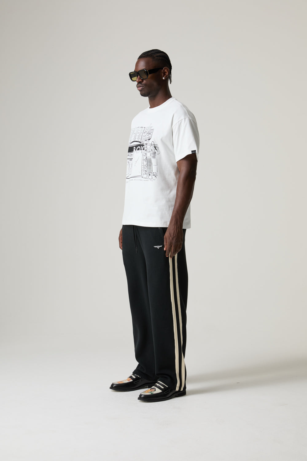 Model wearing a BOY LONDON white t-shirt and black pants with white stripes on a plain background