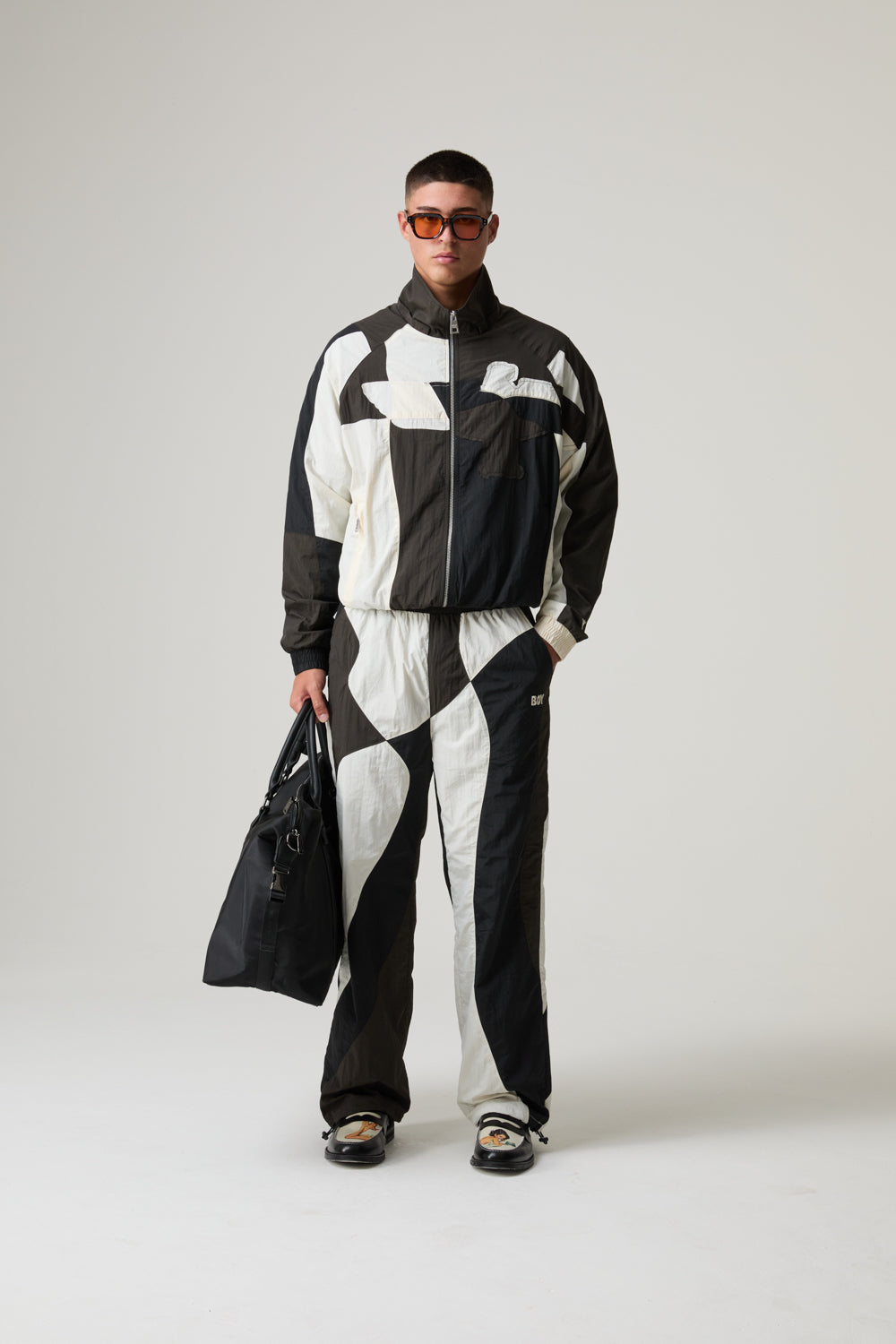 Model wearing a black and white BOY LONDON checkered outfit with sunglasses on a plain background