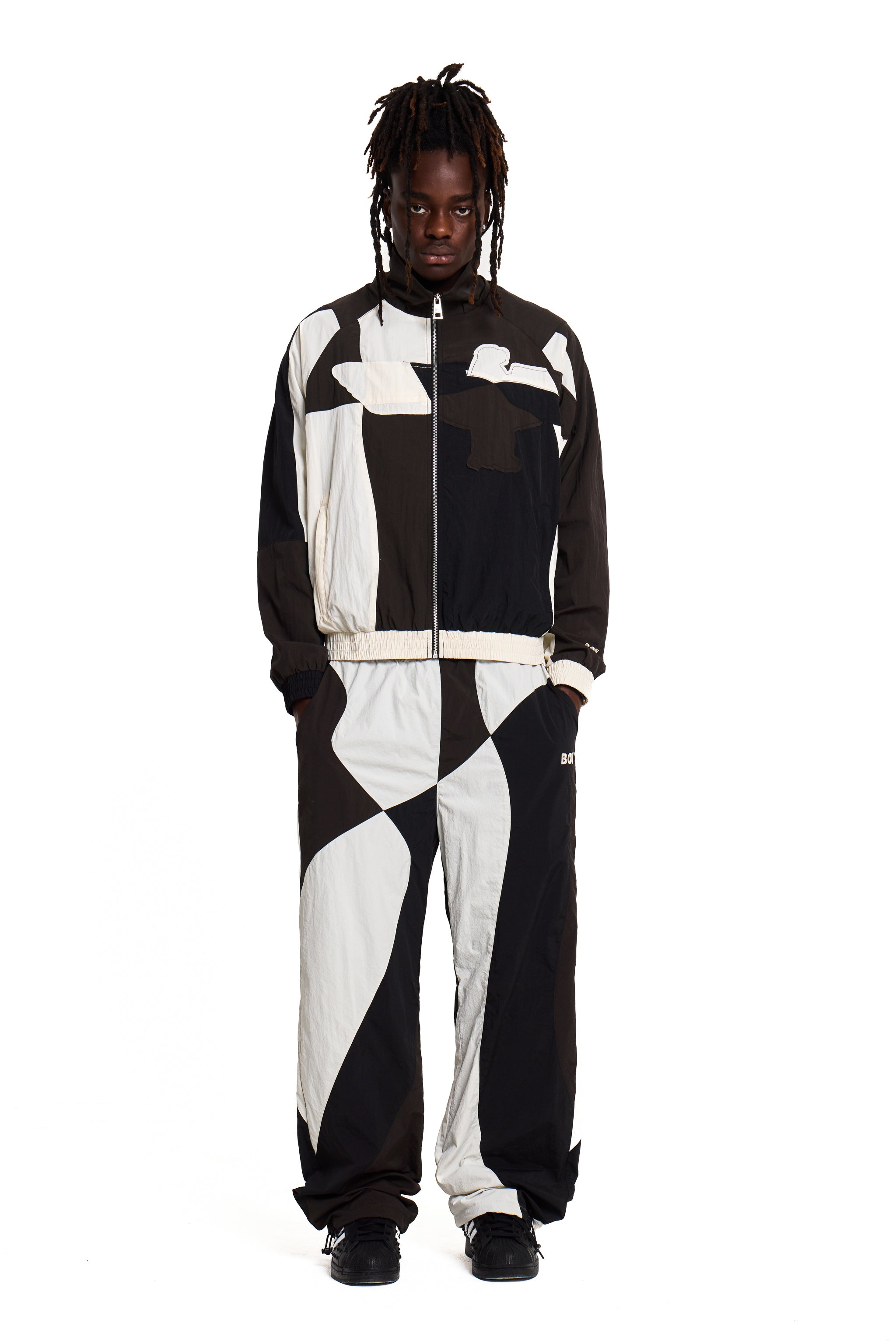 Person wearing a black and white Boy London geometric-patterned tracksuit on a white background
