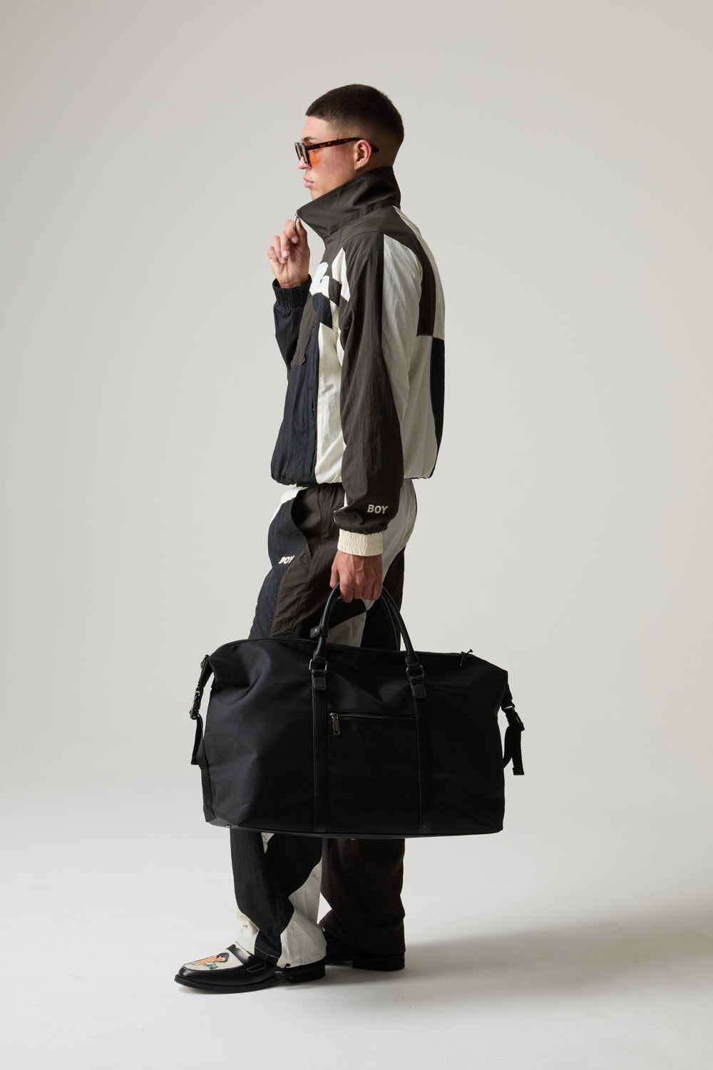 Model wearing a BOY LONDON outfit, holding a black duffel bag against a plain background