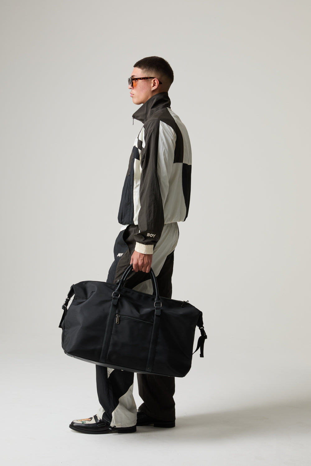 Model wearing a BOY LONDON outfit,  holding a black duffel bag against a plain background