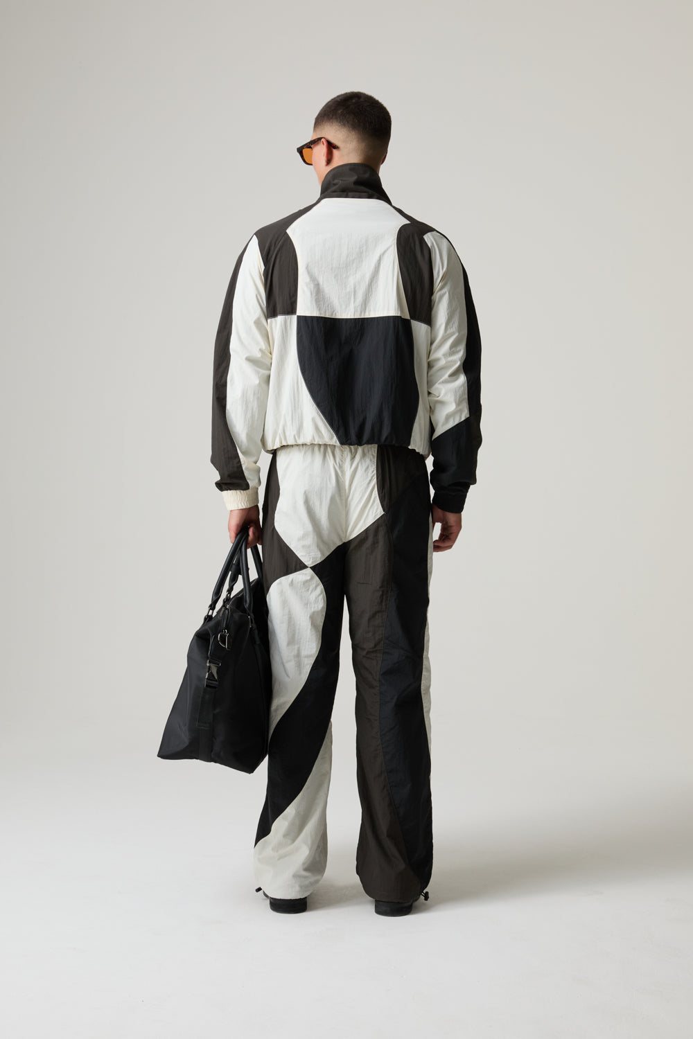Model wearing a black and white BOY LONDON checkered outfit holding a black bag on a plain background