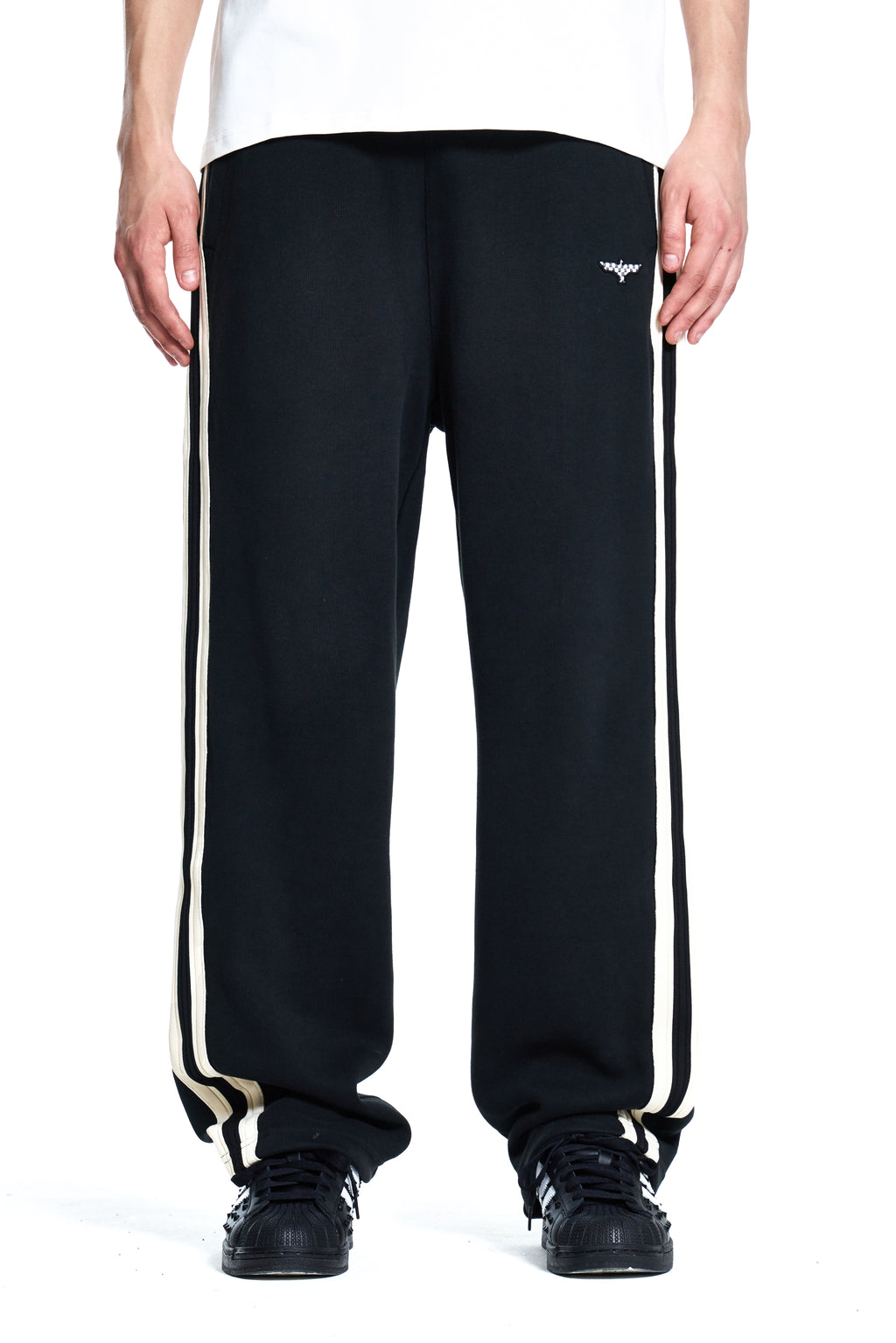 Black track pants with white stripes worn by a person on a white background