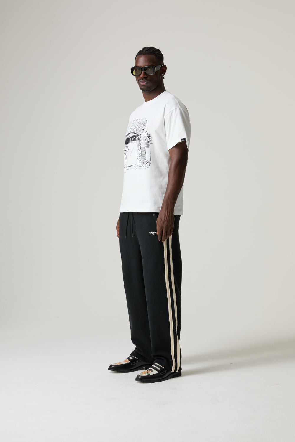 Model wearing a white BOY LONDON t-shirt and black pants with stripes on a plain background