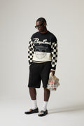 Model wearing a black and white BOY LONDON checkered sweater with text, black shorts, and holding a bag on a plain background