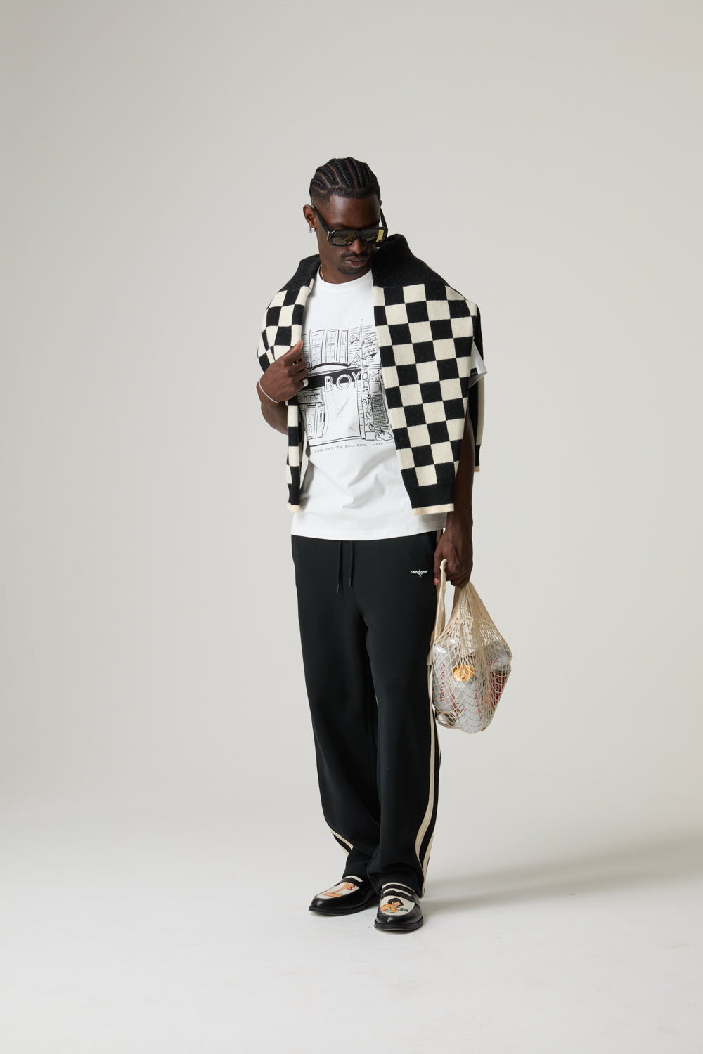 Model wearing a BOY LONDON checkered jacket, white shirt, black pants, and sandals on a plain background